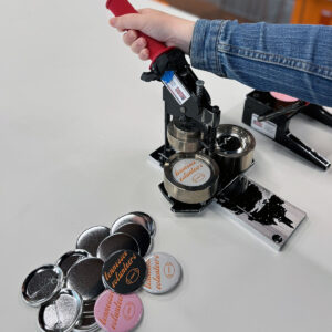 person with their hand on a button maker with buttons laying on the table