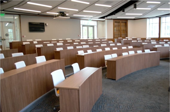 Tiered rows of white rolling chairs positioned behind stationary wood desks.