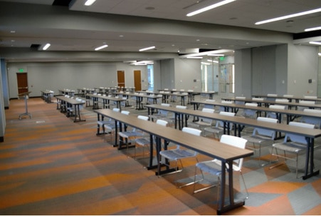 A very large open room with rows of tables and chairs facing a podium at the front.