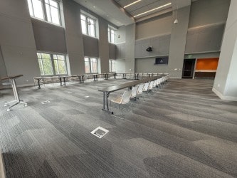 A large open room with high ceilings and windows around 3 sides. Tables and chairs are arranged in a U-shape facing a podium and presentation screen.