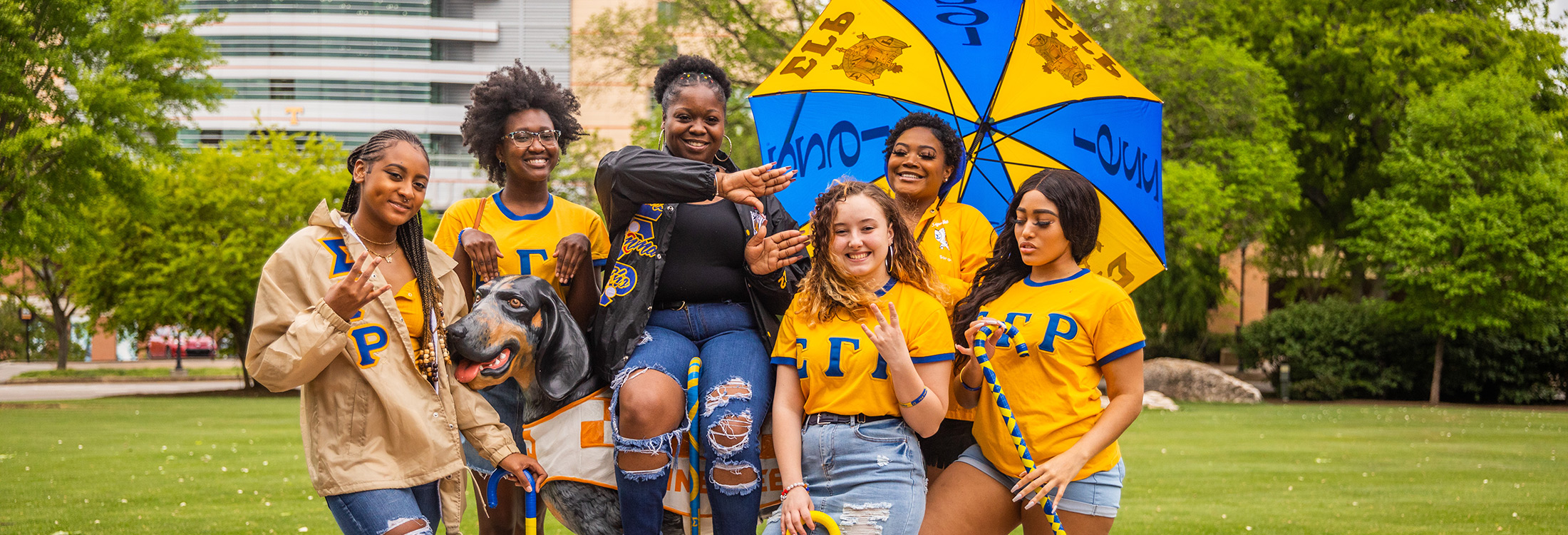 Members of Sigma Gamma Rho sorority pose in Circle Park with a Smokey mascot statue.