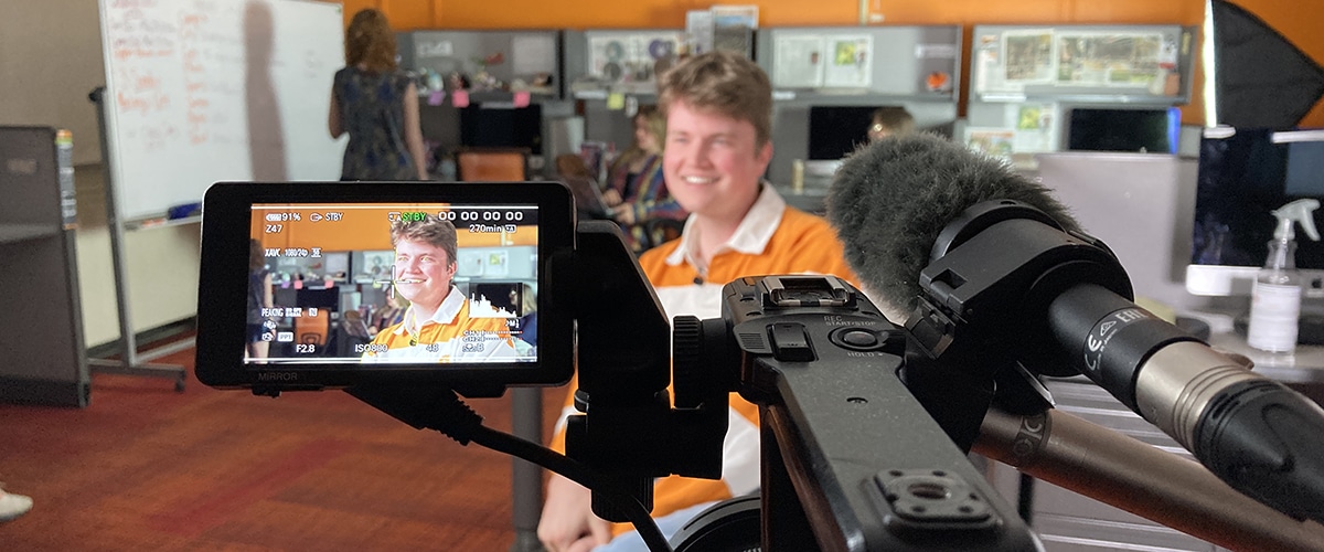 Student in an orange shirt getting interviewed on a camera