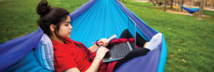A student sits outside with their laptop