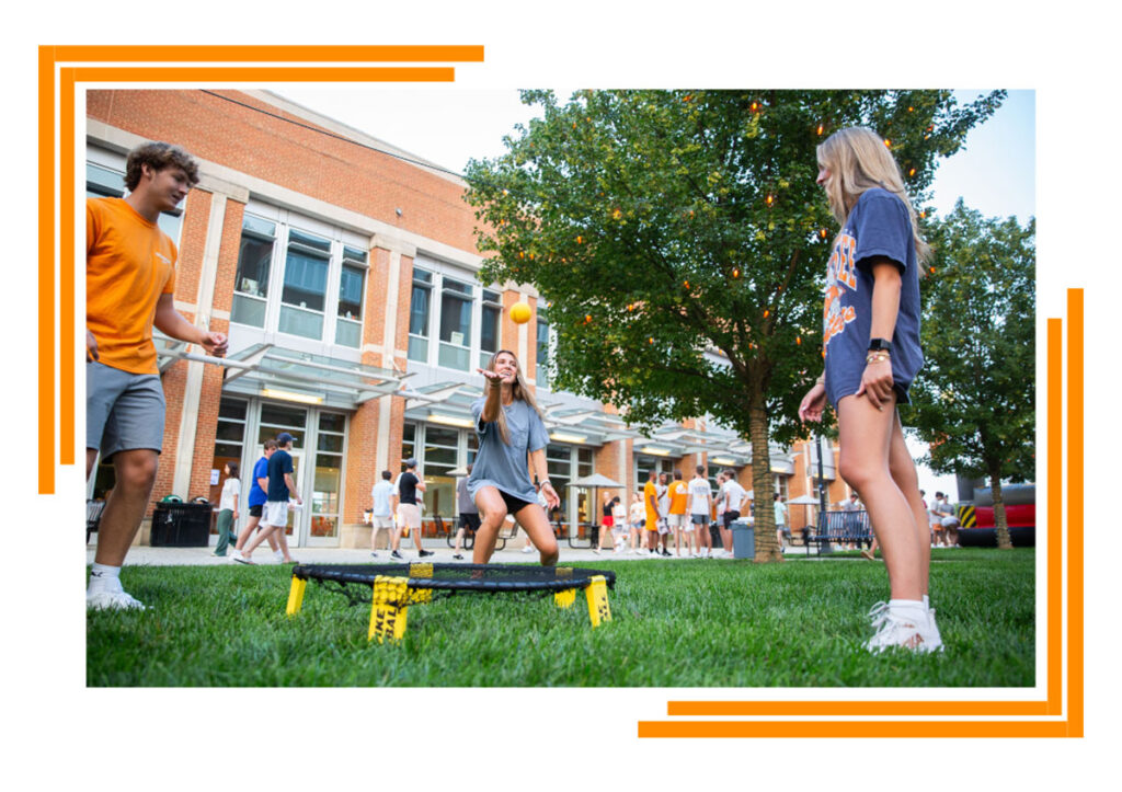 Two female and one male student playing Spikeball outside of the Student Union