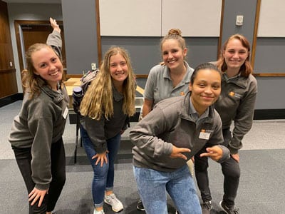 Picture of 5 individuals posing at the student union all wearing some sort of grey shirt.