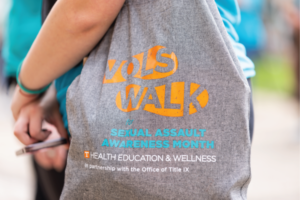 A person holding a tote bag with the Vols Walk for Sexual Assault Awareness Month logo printed on the side.