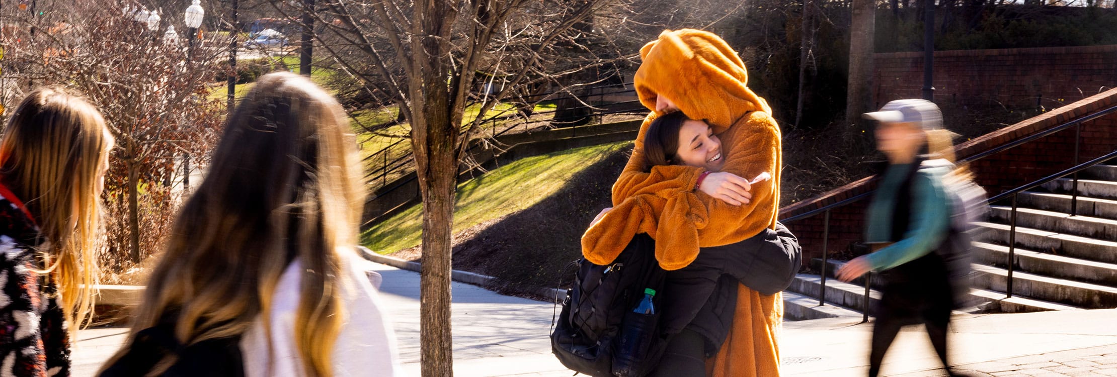 Student receives a hug while passing out suckers along Ped walkway while dressed in a Tenderheart Care Bear costume.