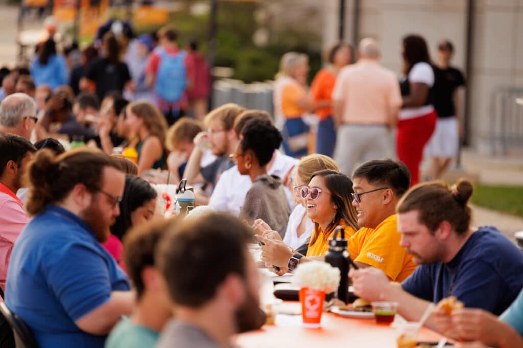 Students sit at a table that stretches pedestrian walkway.