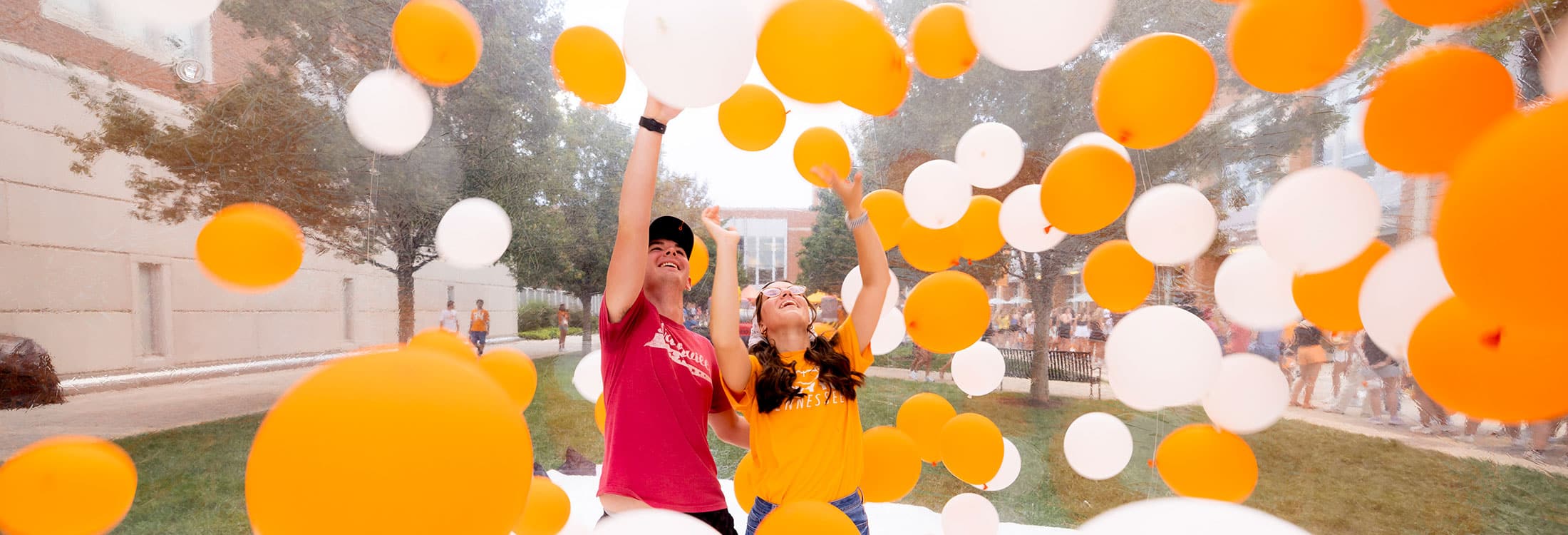 Two people interact with orange and white balloons.