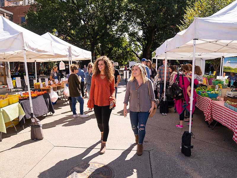 Two students walk between stalls at the farmers market in Market Square.