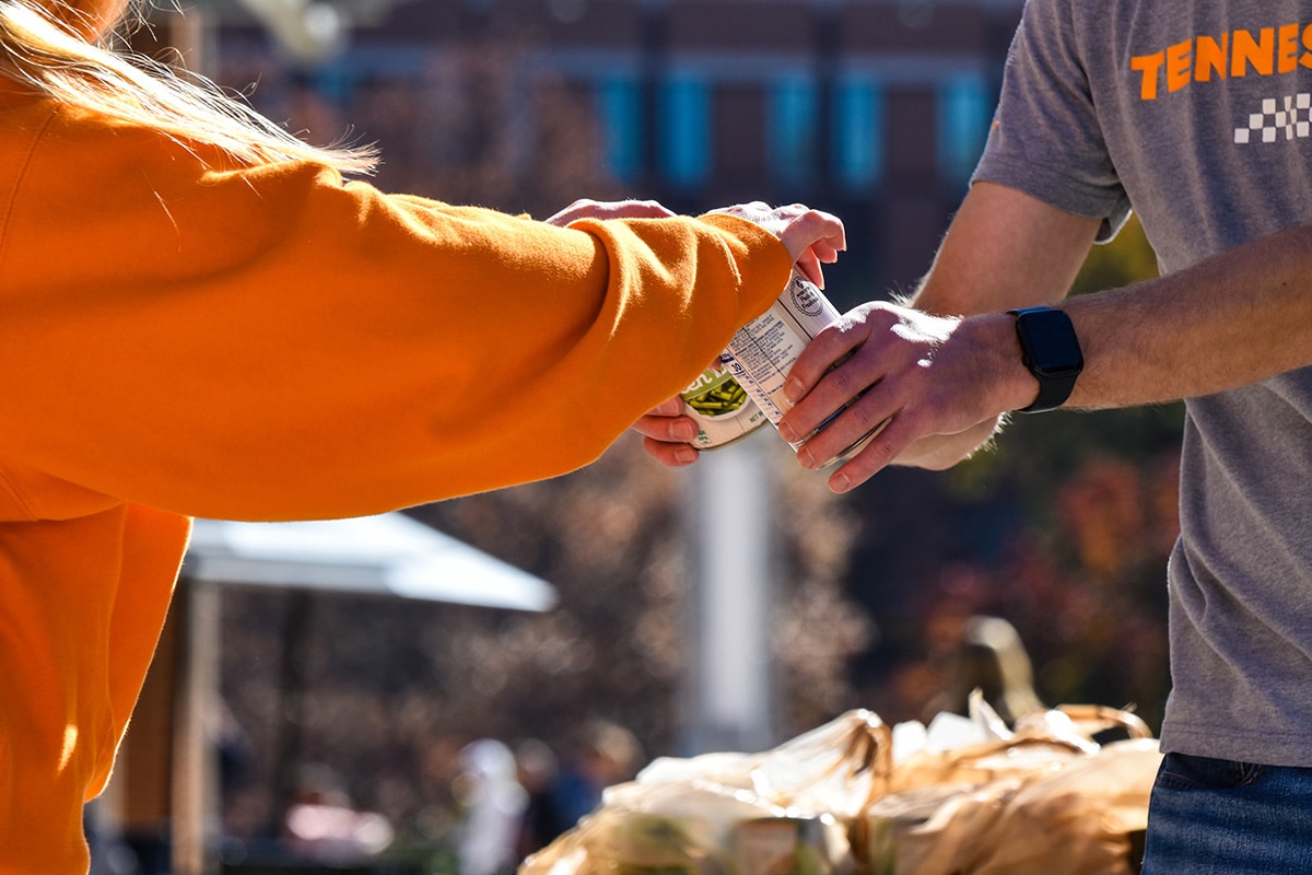 a student in an orange sweater ands another student a can of food