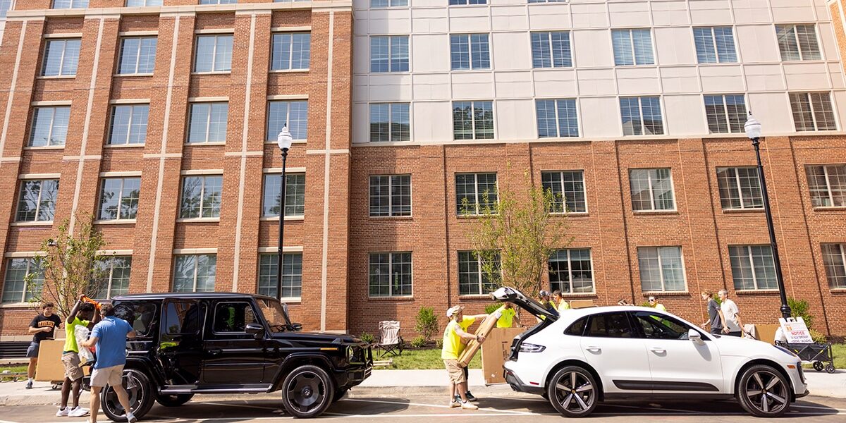 two cars with people unloading boxes parked in front of a residence hall on move-in day