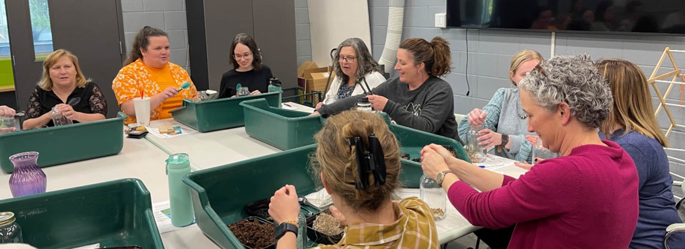a group of Be Well program attendees sit at a large table and build a terrarium 
