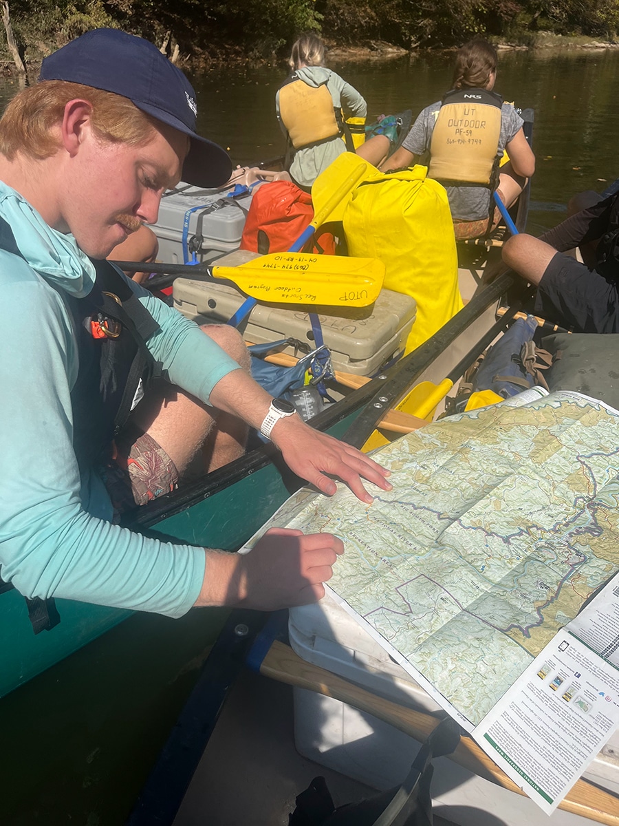 person writes on a map while others behind look at the river